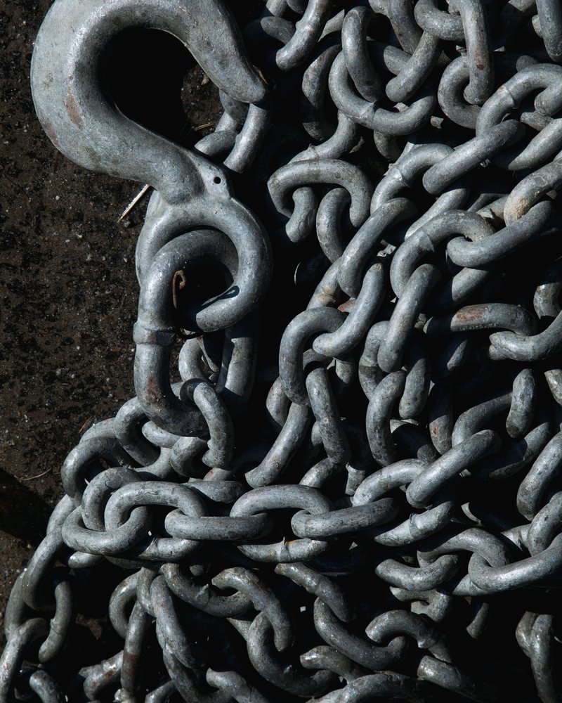 A coiled tow chain and a forged hook on pavement.