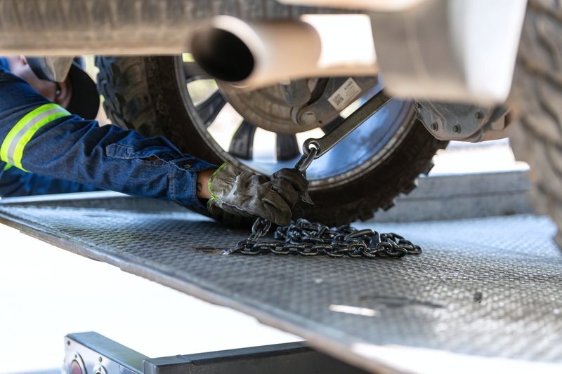 An operator reaching under a vehicle to run a chain to the wheel.