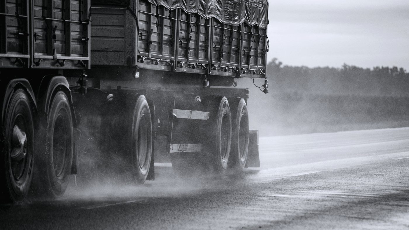 A heavy truck throwing spray from its drive tires on a rain-soaked highway.
