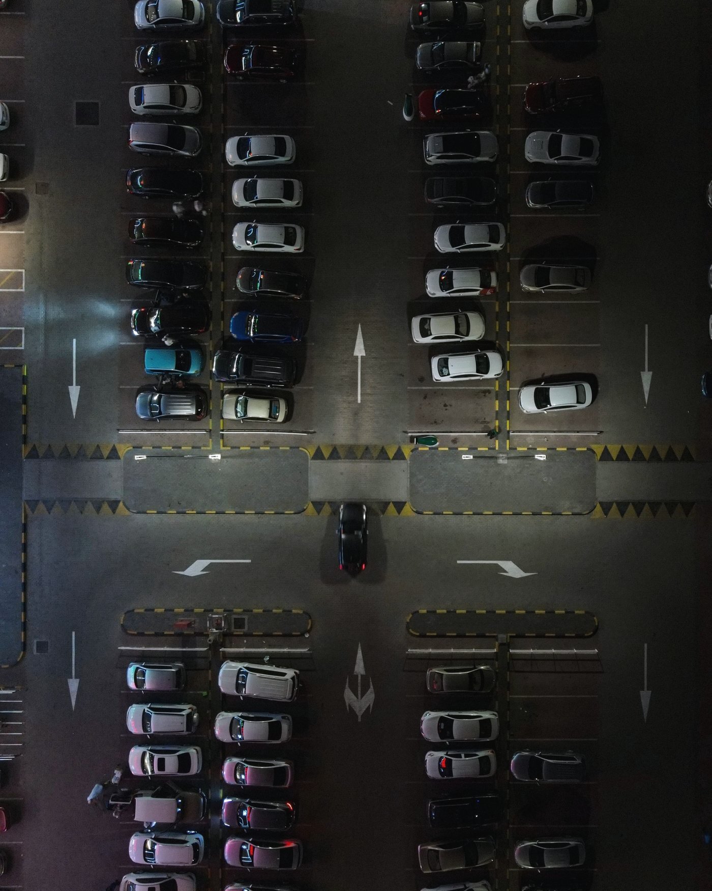 Overhead view of vehicles parked in marked rows under lot lighting at night.