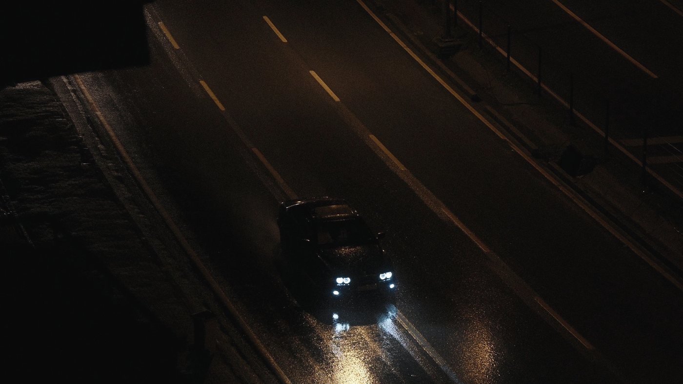 A single vehicle on a wet highway at night, lit only by its own headlights.